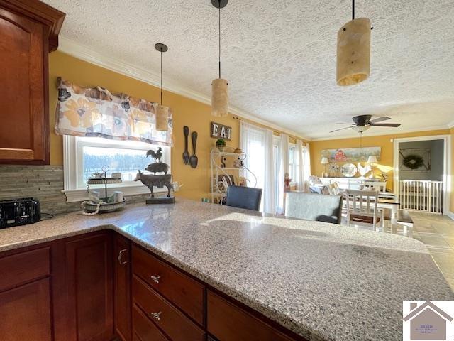 kitchen with a healthy amount of sunlight, light stone countertops, ornamental molding, and open floor plan