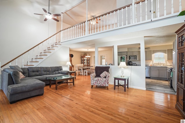 living area featuring light wood-type flooring, a towering ceiling, and ceiling fan with notable chandelier