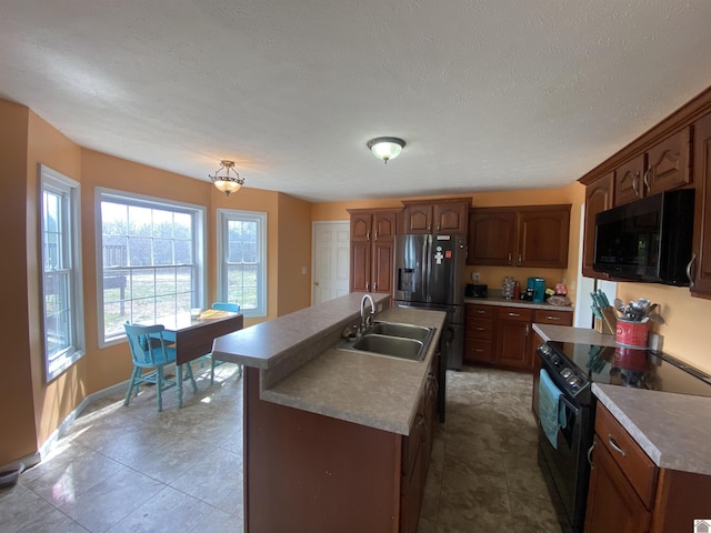 kitchen featuring a textured ceiling, tile patterned flooring, a sink, black appliances, and an island with sink