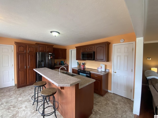 kitchen featuring a breakfast bar, light countertops, a kitchen island with sink, a sink, and black appliances