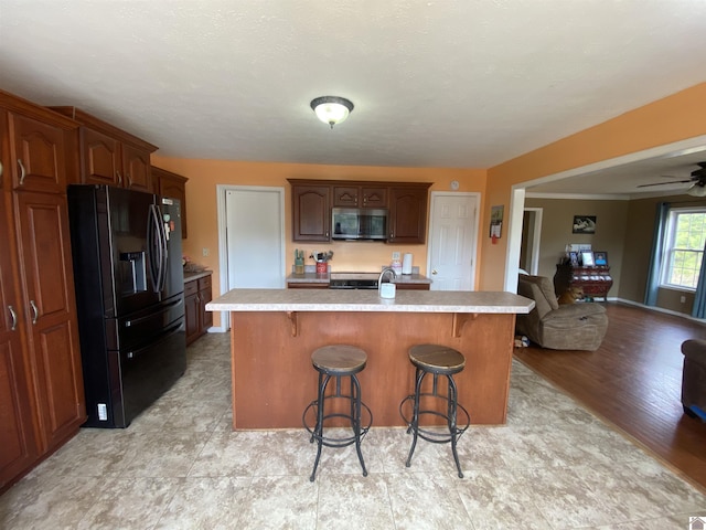 kitchen featuring a breakfast bar, stainless steel microwave, black refrigerator with ice dispenser, and light countertops