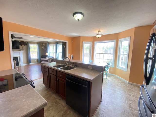 kitchen featuring a fireplace, a sink, open floor plan, freestanding refrigerator, and dishwasher