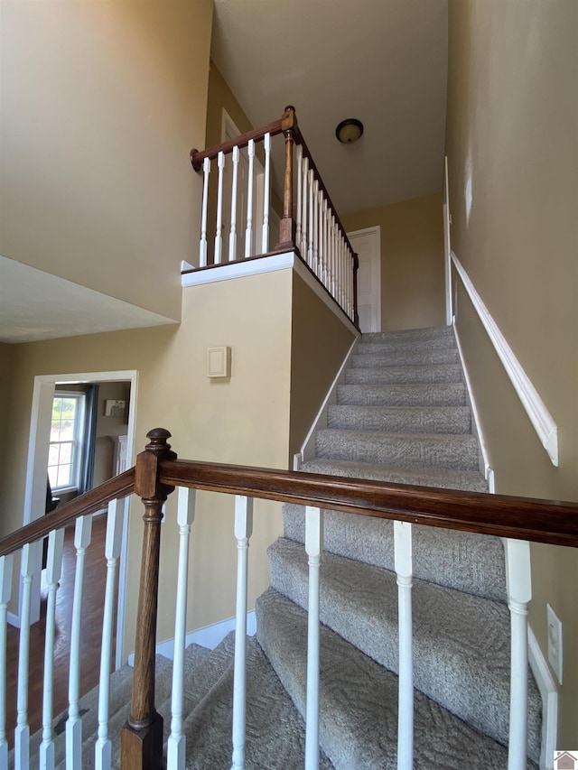 staircase featuring a towering ceiling, baseboards, and wood finished floors