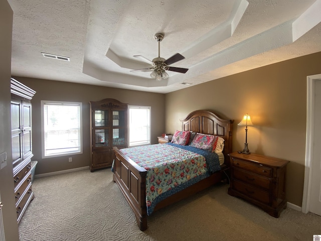 bedroom featuring a textured ceiling, a tray ceiling, visible vents, and baseboards