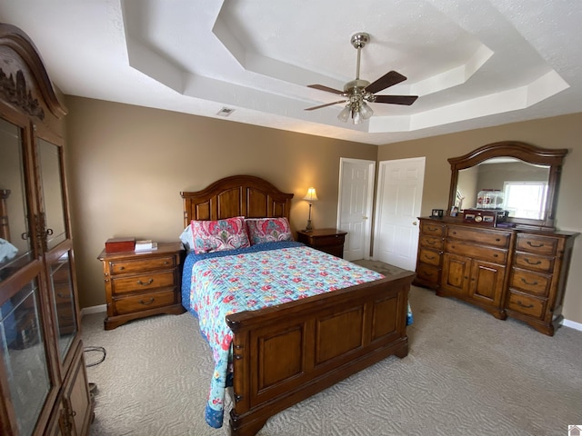 bedroom with light carpet, ceiling fan, a tray ceiling, and visible vents