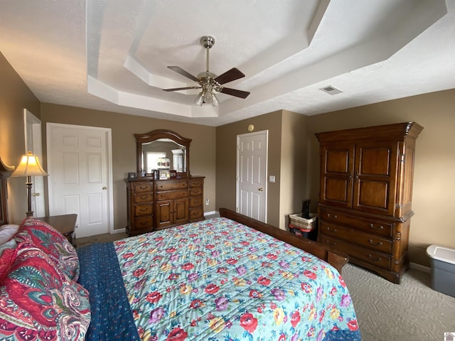 carpeted bedroom with a tray ceiling, visible vents, a ceiling fan, a textured ceiling, and baseboards