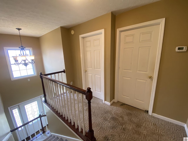 staircase with baseboards, a textured ceiling, carpet flooring, and a notable chandelier