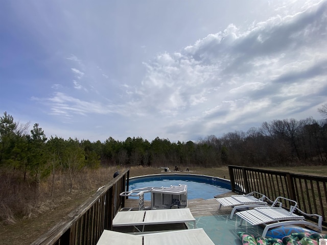 view of swimming pool featuring a wooden deck and a view of trees