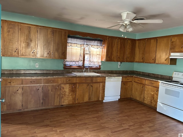 kitchen with white appliances, dark countertops, a sink, and under cabinet range hood