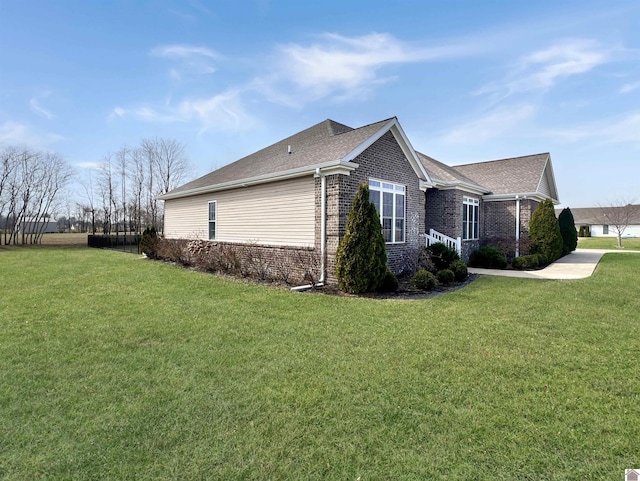 view of side of property featuring a yard, brick siding, and a shingled roof