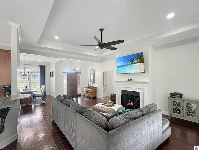 living area with dark wood-style floors, a lit fireplace, a raised ceiling, and crown molding