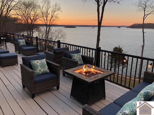 deck at dusk featuring a water view and an outdoor living space with a fire pit