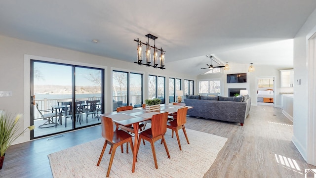 dining area featuring light wood-style flooring, a fireplace, visible vents, and vaulted ceiling