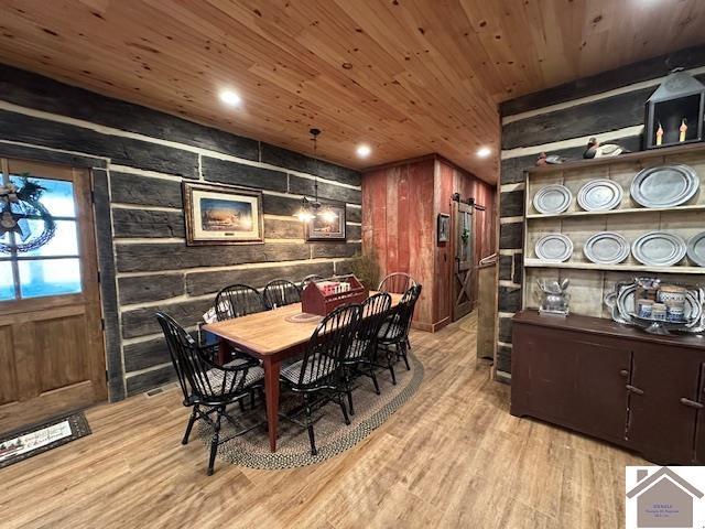 dining space with light wood-type flooring, wood ceiling, wood walls, and a barn door