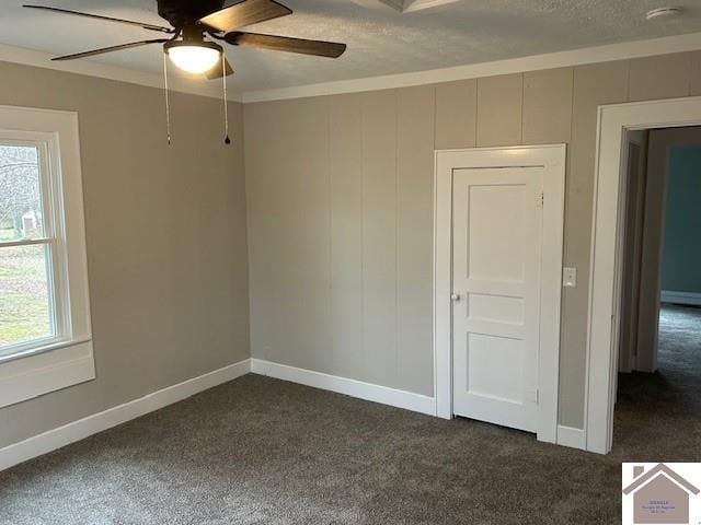 empty room with dark colored carpet, ceiling fan, a textured ceiling, and baseboards