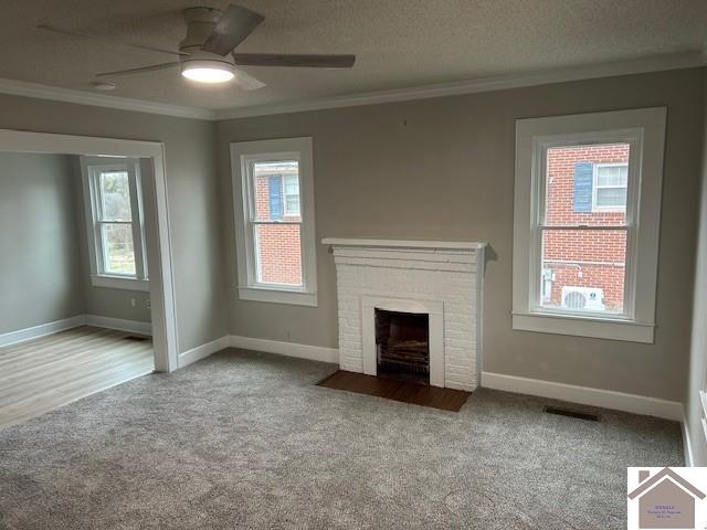 unfurnished living room featuring a brick fireplace, visible vents, a textured ceiling, and ornamental molding