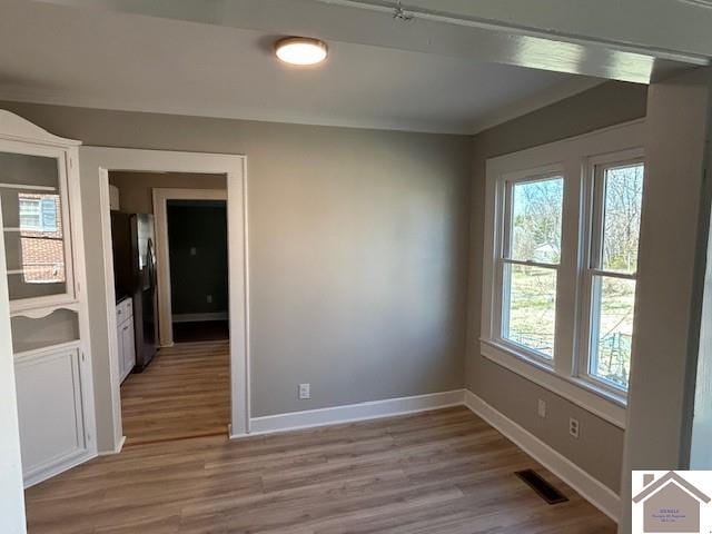 spare room with light wood finished floors, baseboards, visible vents, and ornamental molding