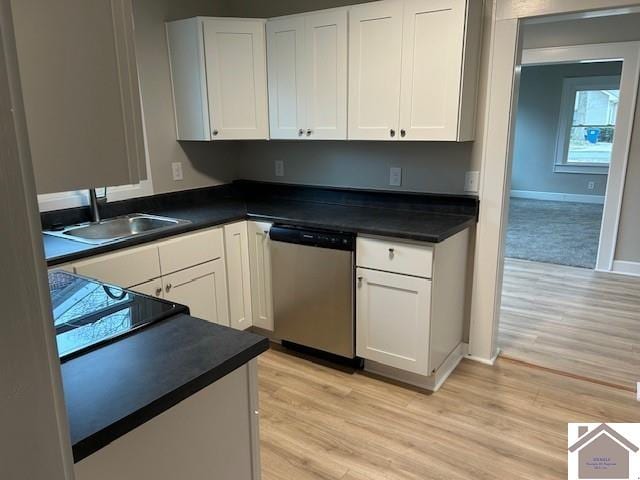 kitchen featuring light wood-style floors, dark countertops, dishwasher, and a sink