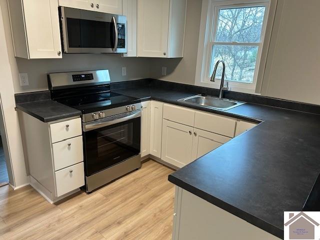 kitchen featuring stainless steel appliances, dark countertops, white cabinets, and a sink