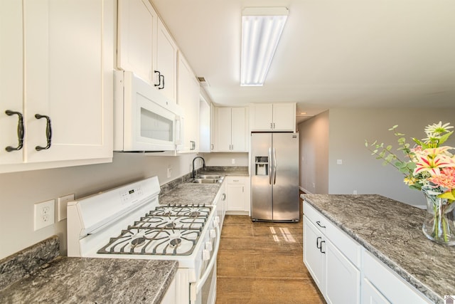 kitchen with dark stone counters, white appliances, white cabinetry, and a sink