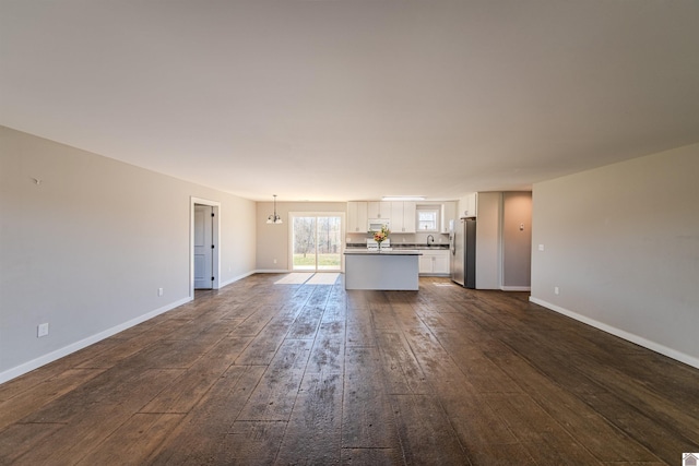 unfurnished living room featuring a sink, baseboards, and dark wood-type flooring