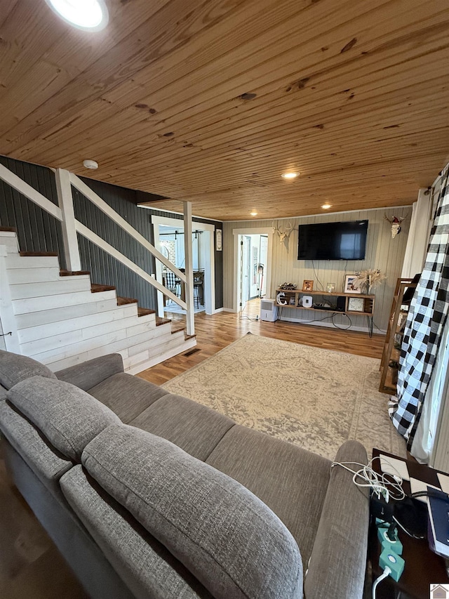 living area with stairs, wood walls, wooden ceiling, and wood finished floors