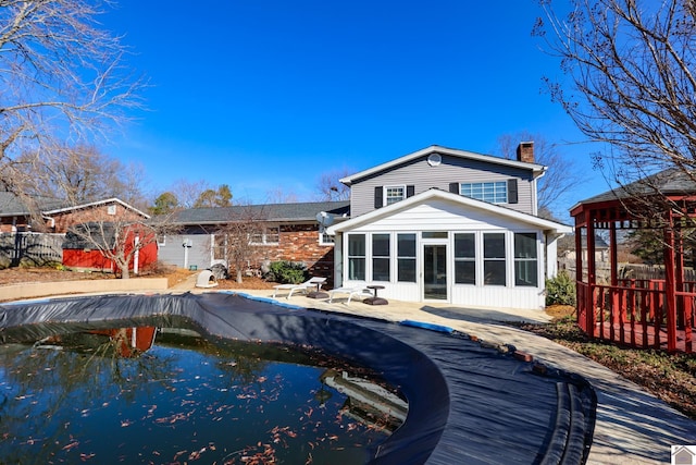 rear view of house featuring a fenced in pool, a sunroom, fence, and a chimney