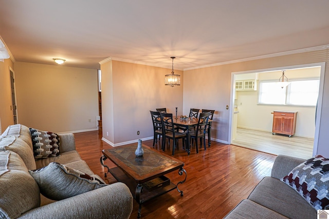 living area with baseboards, wood-type flooring, a chandelier, and crown molding