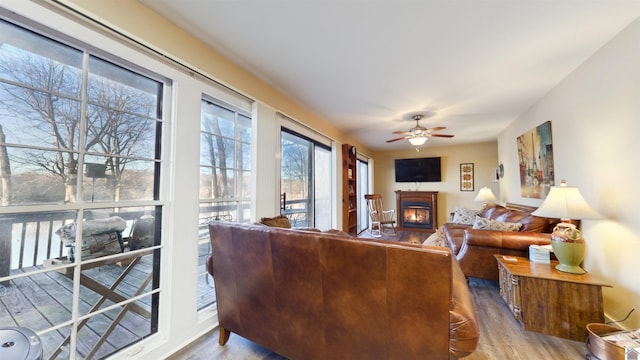 living room featuring a warm lit fireplace, a ceiling fan, and wood finished floors