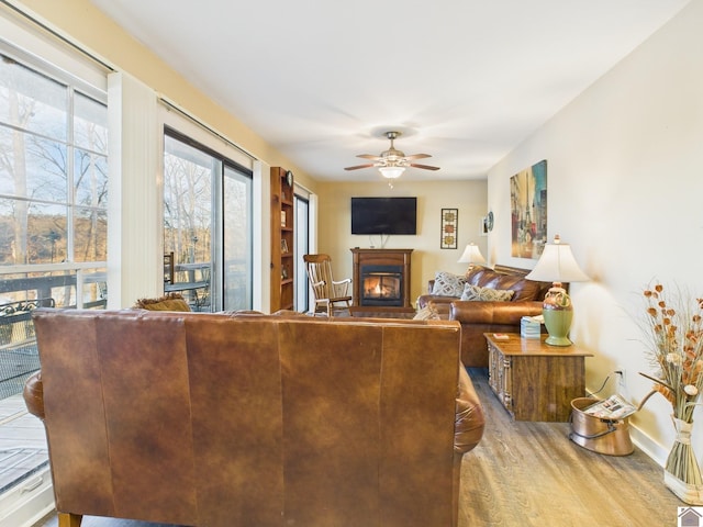 living area with a lit fireplace, baseboards, a ceiling fan, and wood finished floors