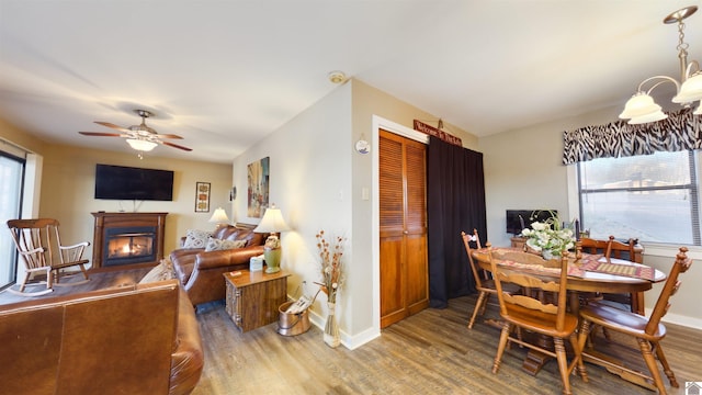 dining room featuring a warm lit fireplace, baseboards, wood finished floors, and a healthy amount of sunlight