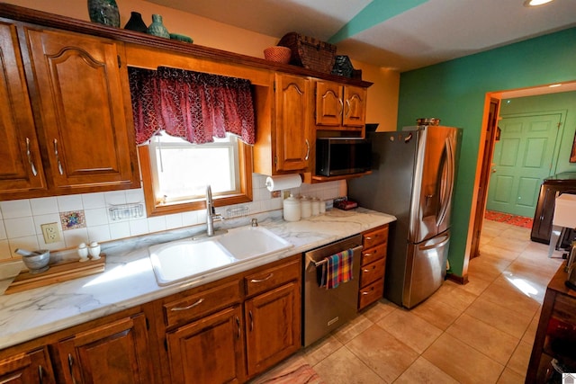 kitchen featuring light tile patterned floors, tasteful backsplash, appliances with stainless steel finishes, brown cabinetry, and a sink