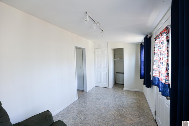 unfurnished bedroom featuring rail lighting, baseboards, and a closet