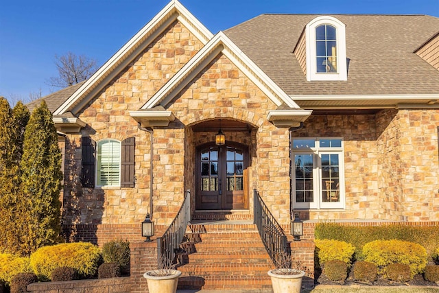 view of front facade featuring stone siding, roof with shingles, and french doors