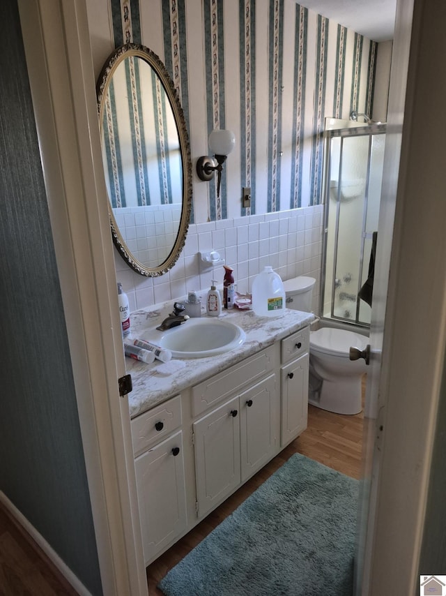 bathroom featuring enclosed tub / shower combo, toilet, wood finished floors, vanity, and wallpapered walls