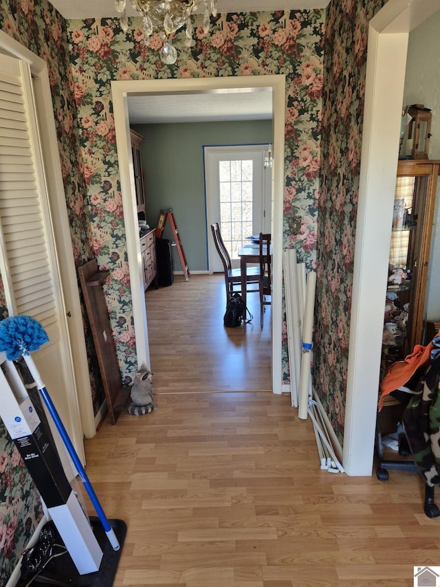 corridor featuring a chandelier, light wood-type flooring, baseboards, and wallpapered walls