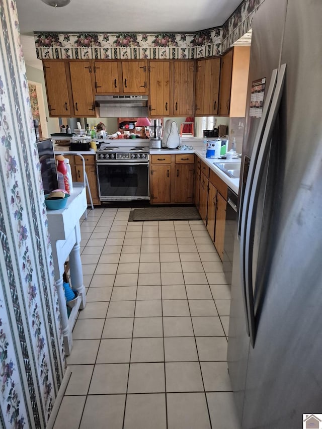 kitchen featuring light tile patterned flooring, under cabinet range hood, light countertops, black appliances, and brown cabinetry