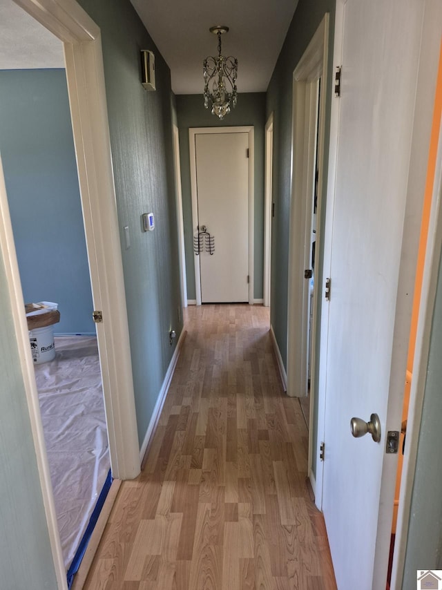 hall with an inviting chandelier, wood finished floors, and baseboards