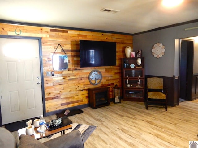 living room with wooden walls, visible vents, wood finished floors, crown molding, and a fireplace