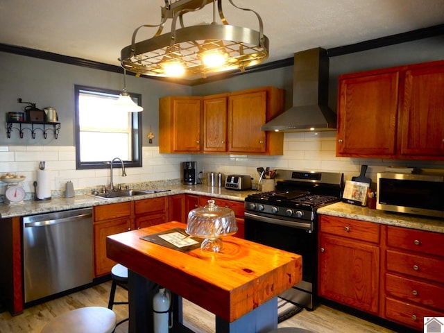 kitchen with tasteful backsplash, light wood-style flooring, appliances with stainless steel finishes, wall chimney range hood, and a sink