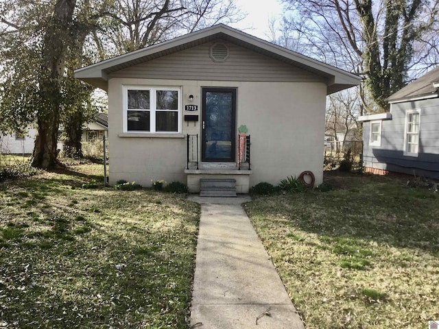 bungalow with entry steps, concrete block siding, and a front lawn