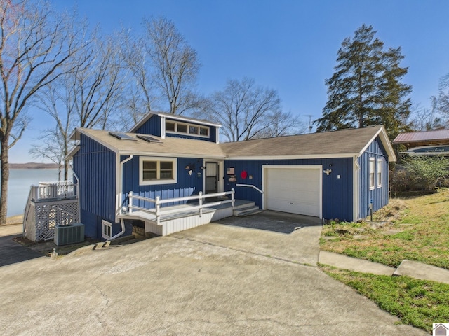 view of front of house with driveway, a garage, central AC unit, a deck with water view, and board and batten siding