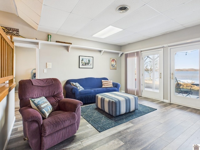 living room with a drop ceiling, wood finished floors, visible vents, and a water view