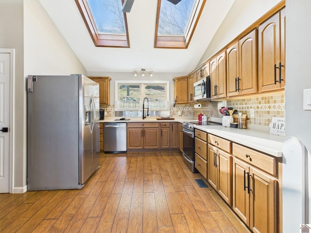 kitchen with lofted ceiling with skylight, stainless steel appliances, light countertops, light wood-type flooring, and a sink