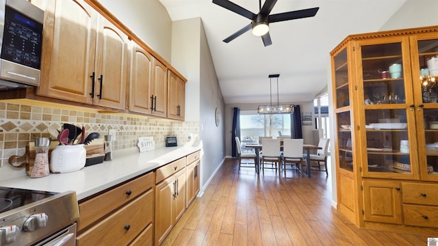 kitchen featuring light wood-style flooring, vaulted ceiling, light countertops, backsplash, and stainless steel microwave