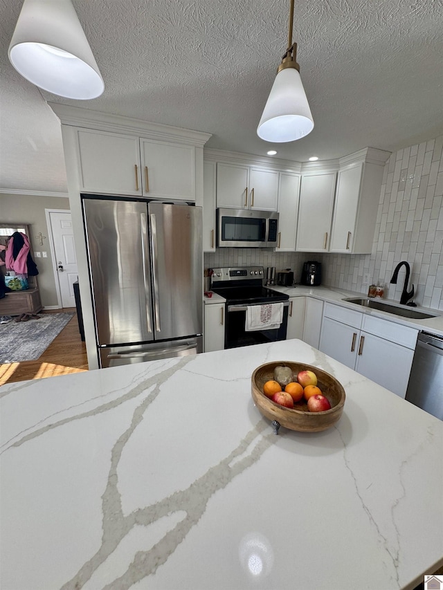 kitchen with white cabinets, decorative backsplash, appliances with stainless steel finishes, pendant lighting, and a sink