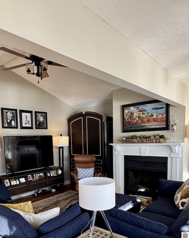 living room featuring vaulted ceiling, ceiling fan, a textured ceiling, and a fireplace