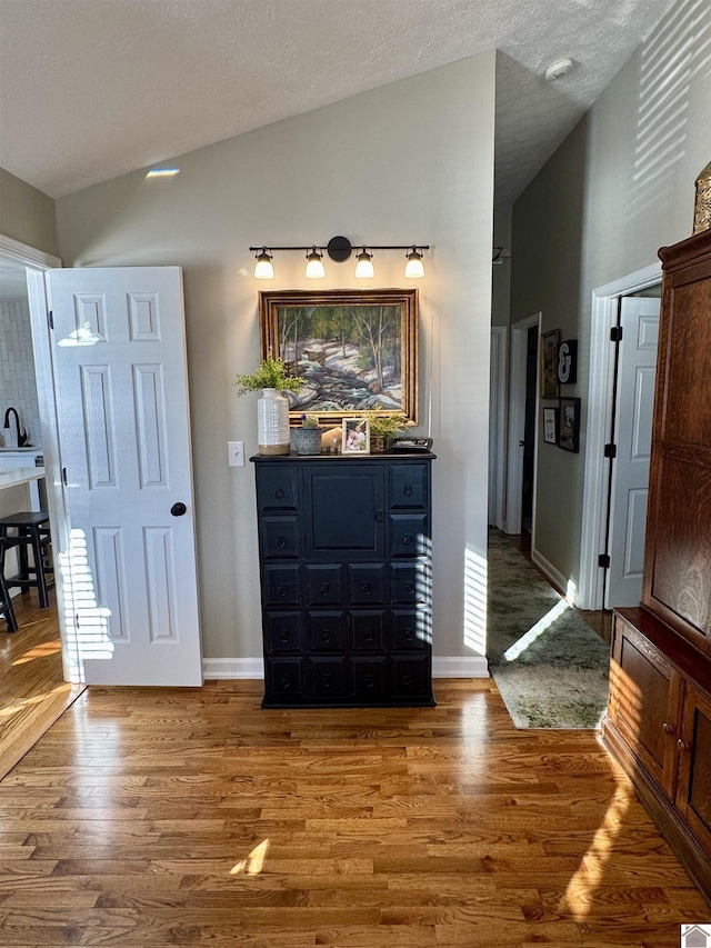 interior space with a textured ceiling, high vaulted ceiling, wood finished floors, and baseboards