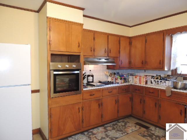 kitchen with stainless steel appliances, brown cabinetry, crown molding, and under cabinet range hood