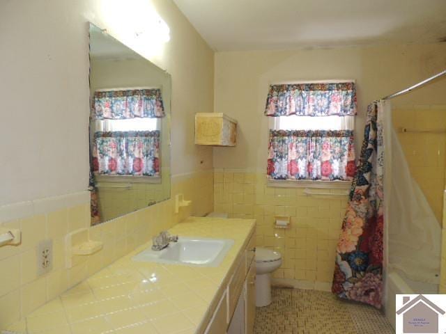 full bathroom featuring wainscoting, toilet, a shower with shower curtain, vanity, and tile walls